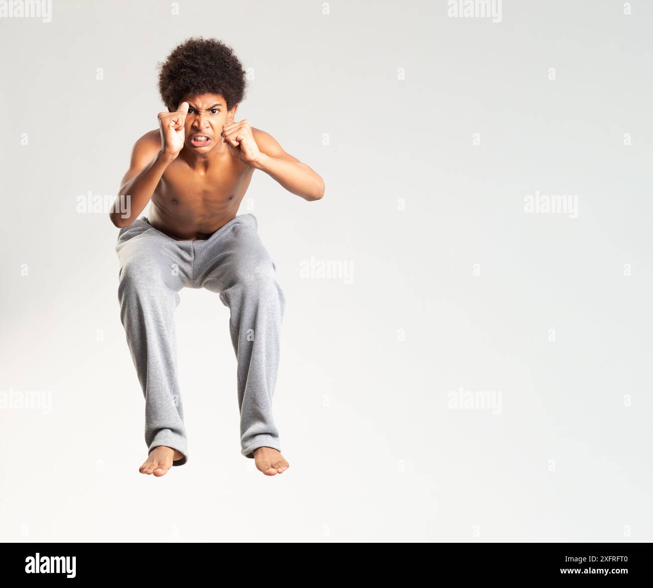 Jeune homme énergique sautant haut, portant un pantalon de survêtement gris décontracté, exprimant l'excitation et le dynamisme. Banque D'Images