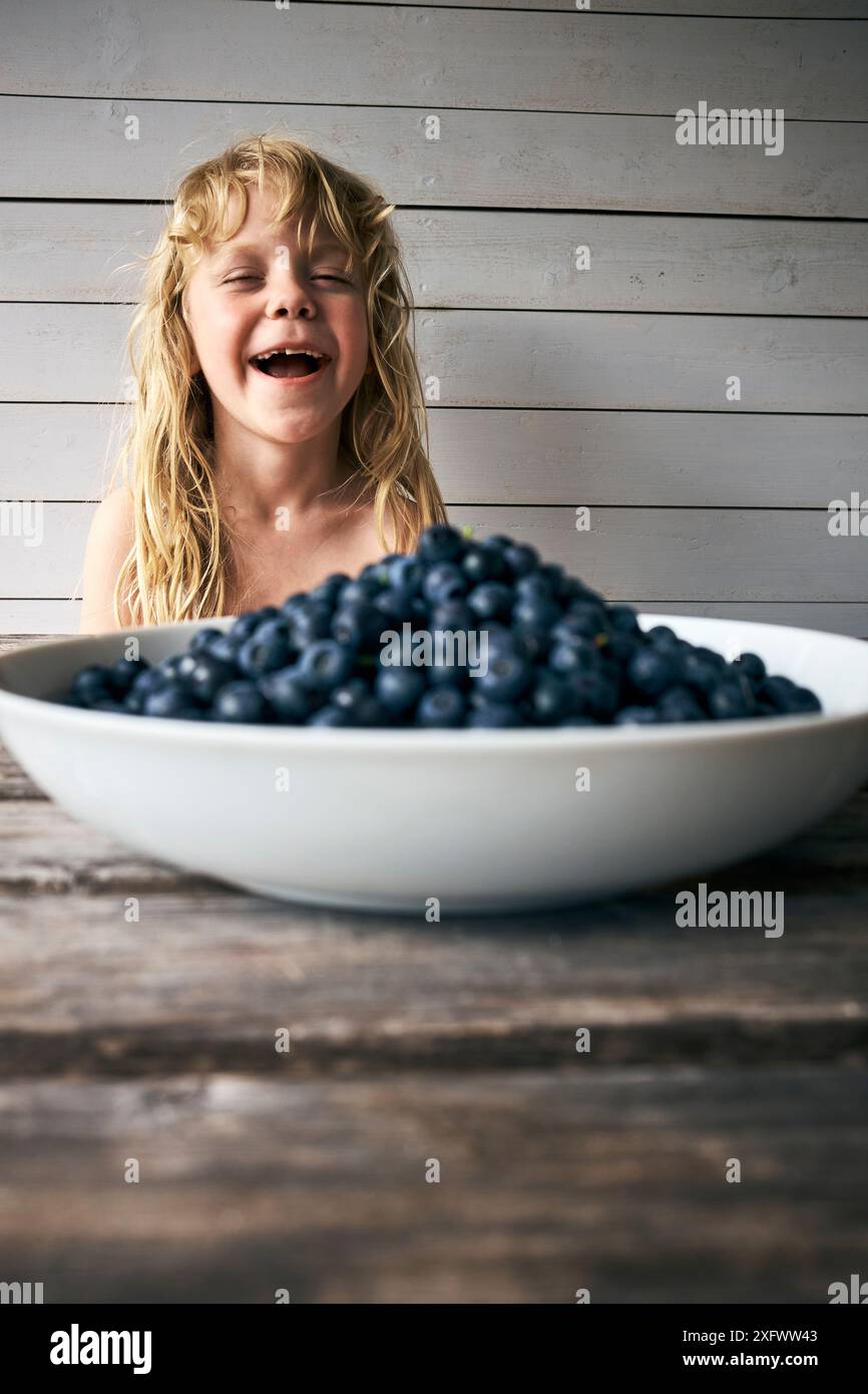 Fille heureuse avec la bouche ouverte regardant un bol de bleuets gardés sur la table Banque D'Images