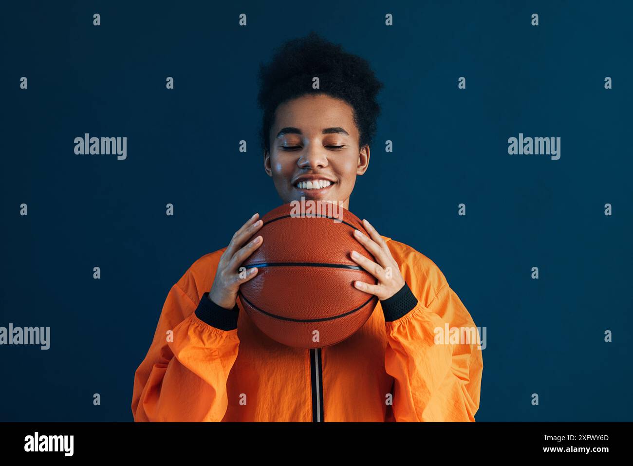 Femme avec basket portant des vêtements de sport orange. Femme souriante avec les yeux fermés tenant un ballon de basket. Femme avec basket-ball portant sportswea orange Banque D'Images