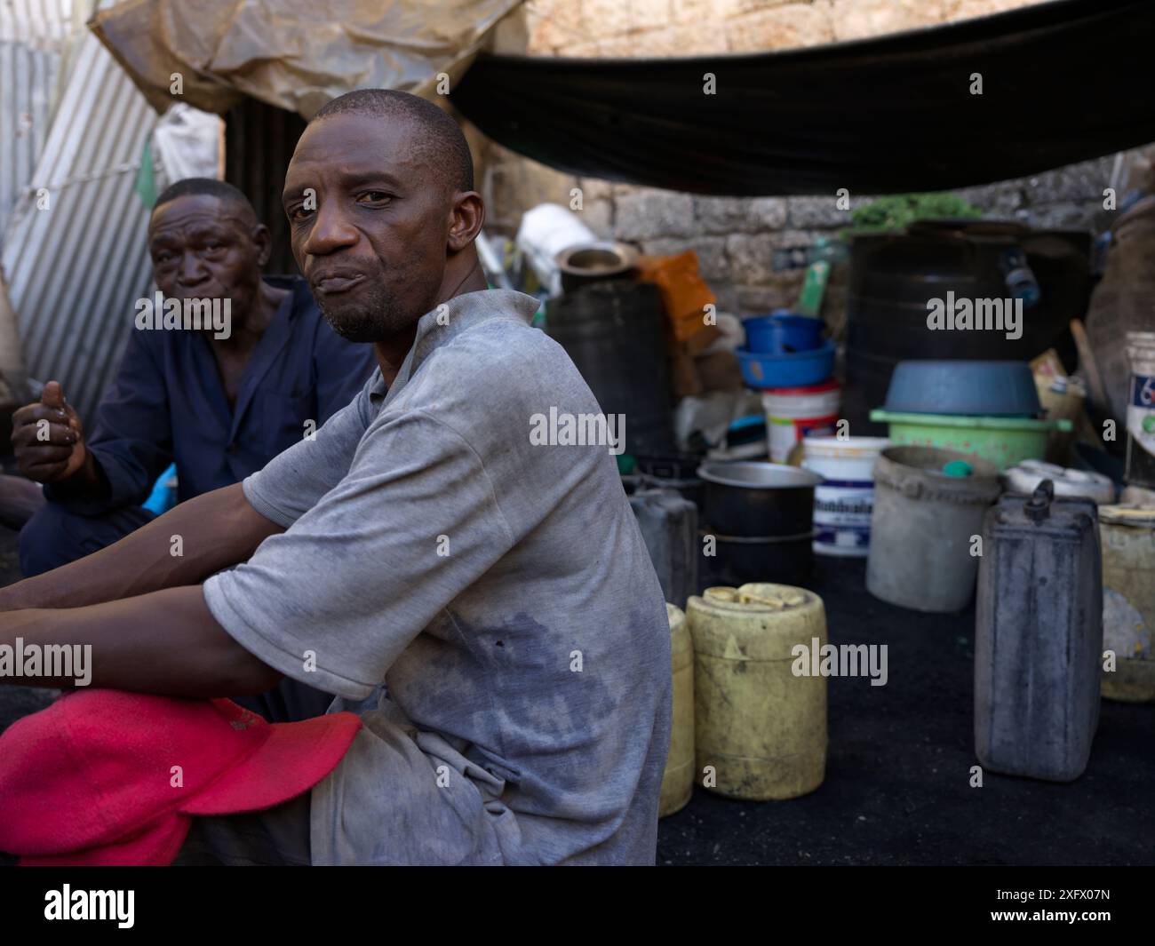 Deux hommes qui font du charbon de bois prenant une pause déjeuner dans leur cour entourés de récipients d'eau Banque D'Images