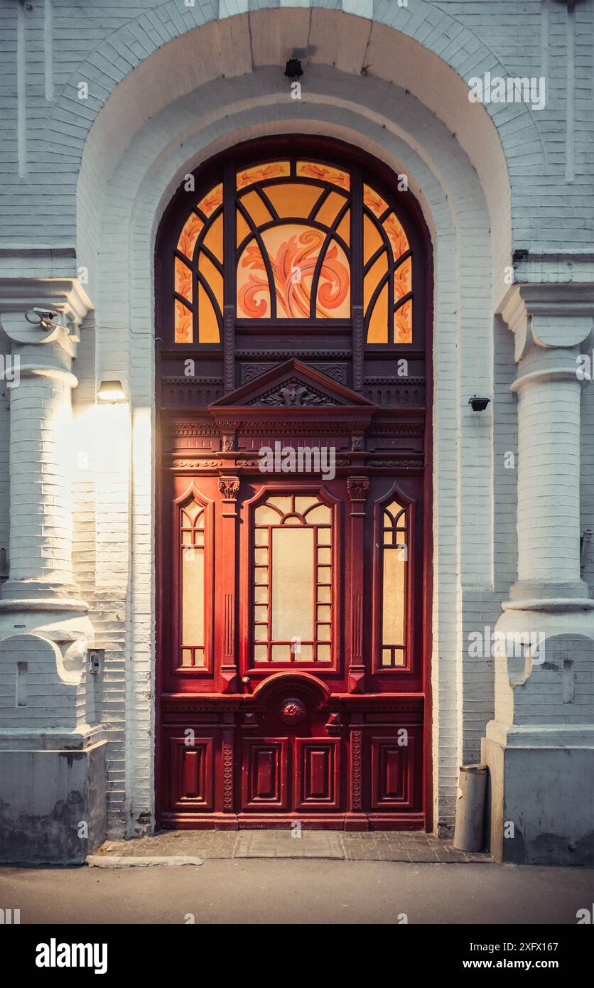 Porte rouge foncé d'une vieille maison. Entrée au bâtiment du 19ème siècle au crépuscule. Porte en bois décorée de vitraux. Banque D'Images