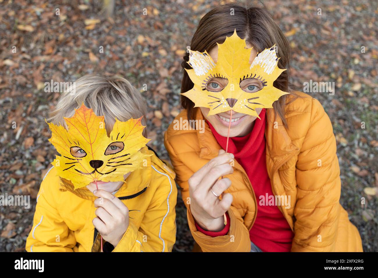 Bonjour, automne. aimez l'automne et la créativité. femme et enfant cachent leurs visages derrière des feuilles d'érable d'automne, sur lesquelles le visage de chat est sculpté. Plaisir dans la nature, Banque D'Images