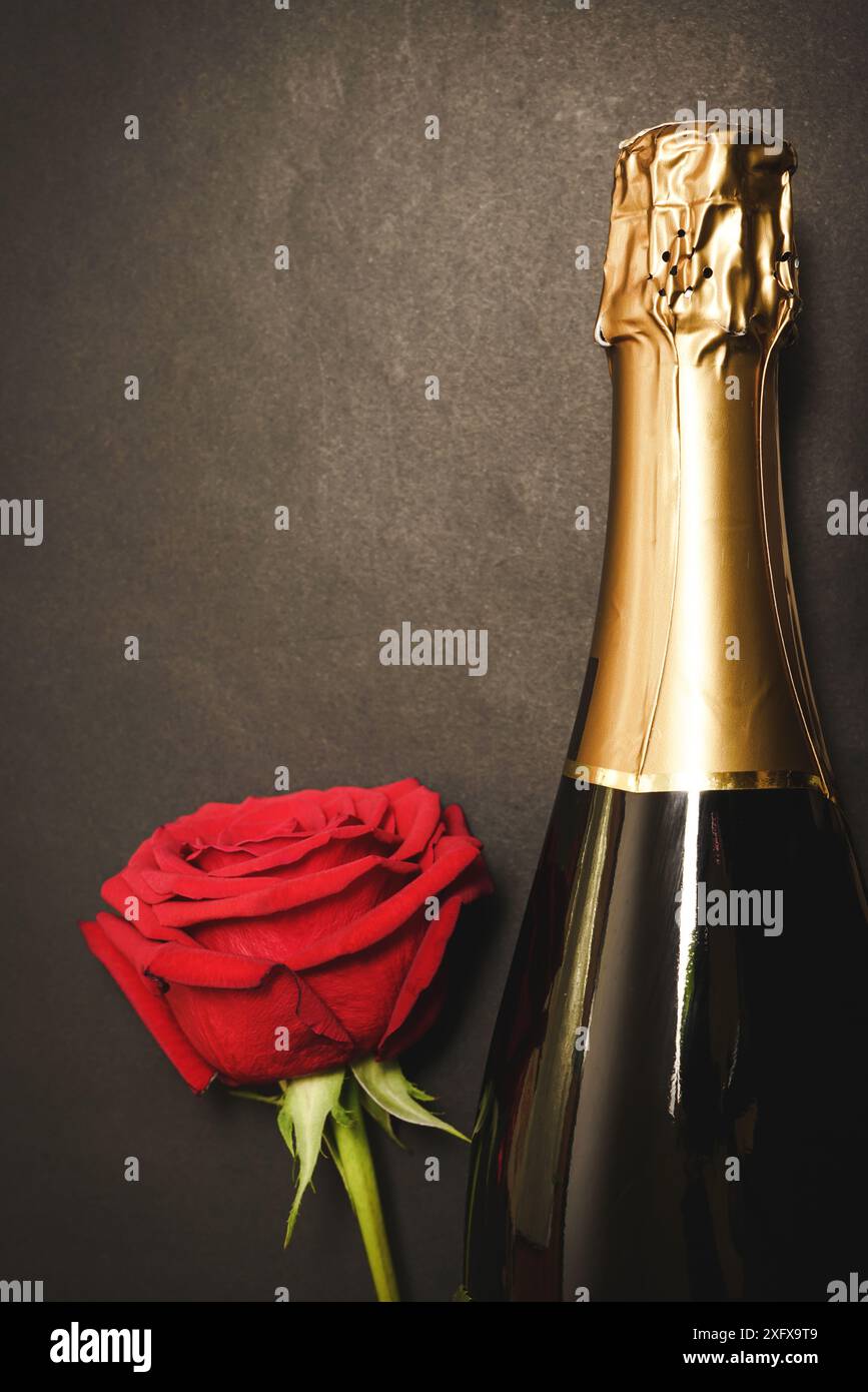 Photo verticale d'une bouteille de champagne et belle rose colombienne rouge dans un élégant fond sombre. Avec espace de copie Banque D'Images