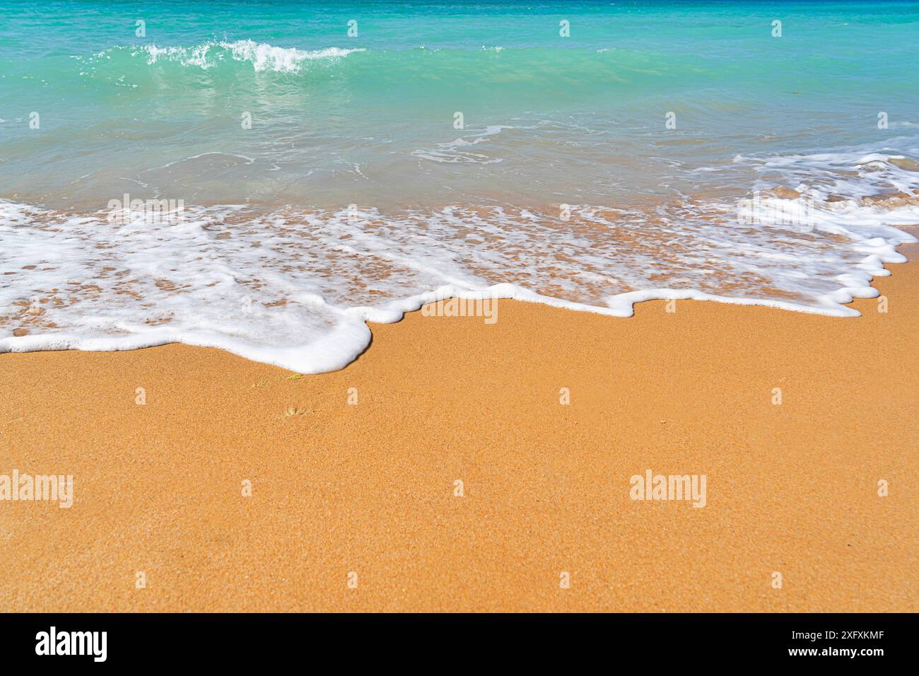 Vagues douces avec mousse laver sur la plage de sable avec de l'eau turquoise claire, créant une scène de bord de mer sereine et relaxante, espace de copie Banque D'Images