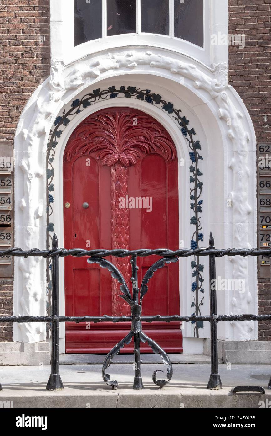 Une porte rouge avec une porte en fer noir devant elle. La porte est décorée de vignes Banque D'Images