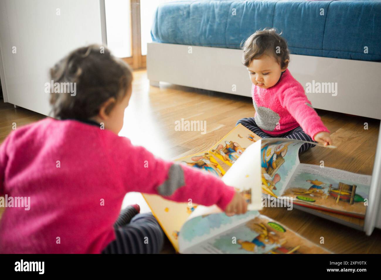 Bébé Enfant fille jouant avec les contes de livre sur le plancher de bois de chêne. Banque D'Images