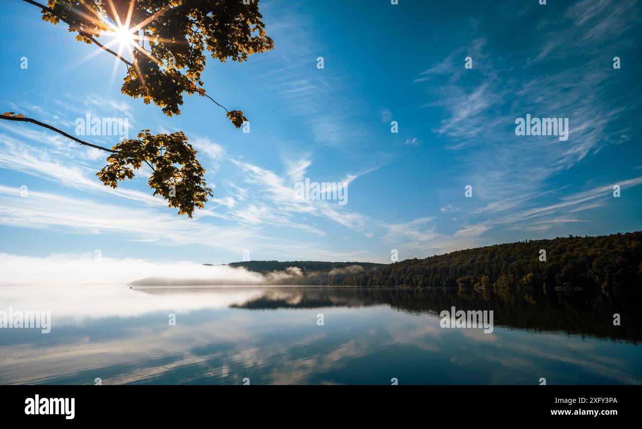 Réservoir du lac Edersee par un matin ensoleillé, léger brouillard au loin, arbres au premier plan, réflexion sur l'eau calme. District de Waldeck-Frankenberg, Hesse, Allemagne. Banque D'Images