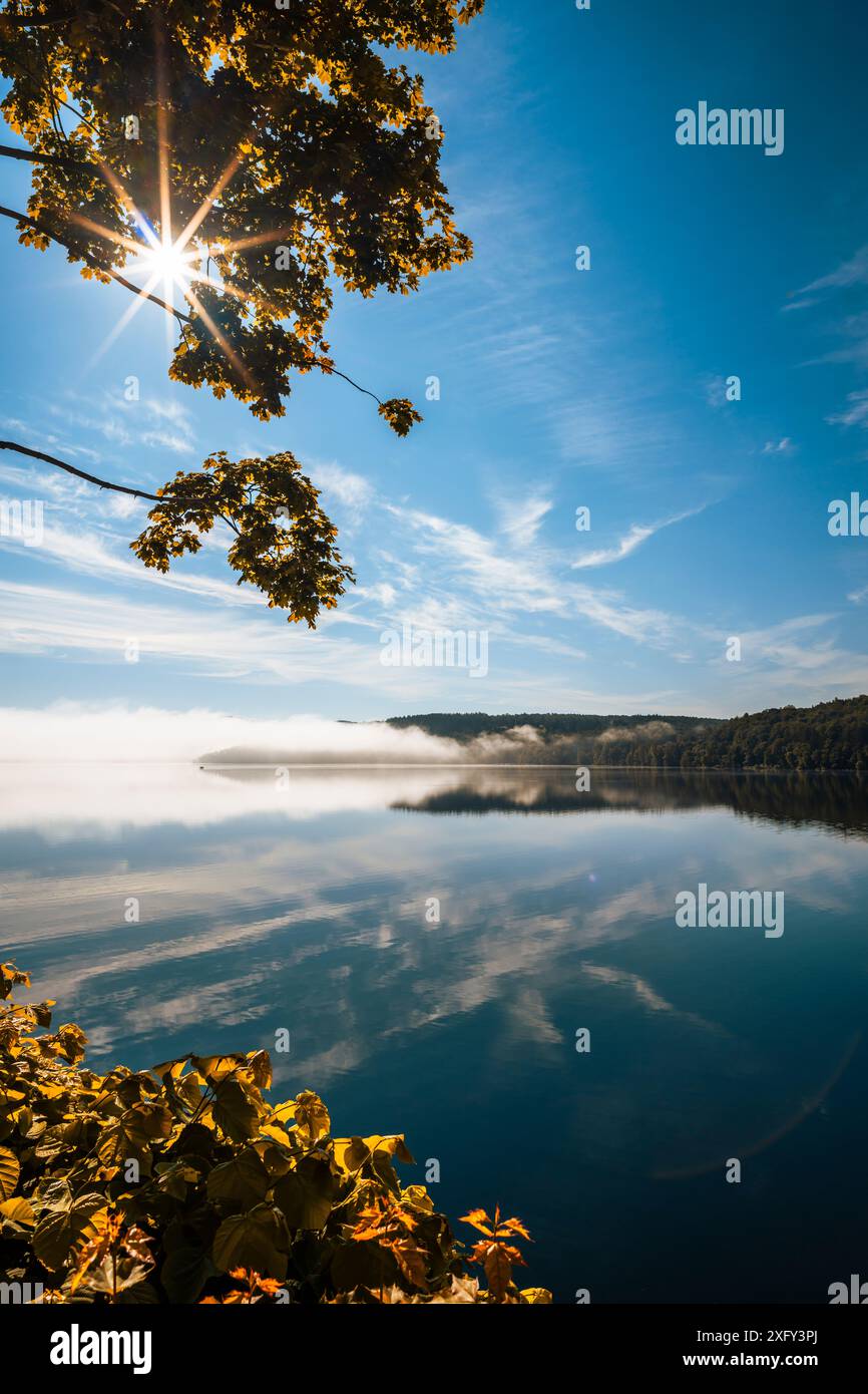 Réservoir du lac Edersee par un matin ensoleillé, léger brouillard au loin, arbres au premier plan, réflexion sur l'eau calme. District de Waldeck-Frankenberg, Hesse, Allemagne. Banque D'Images