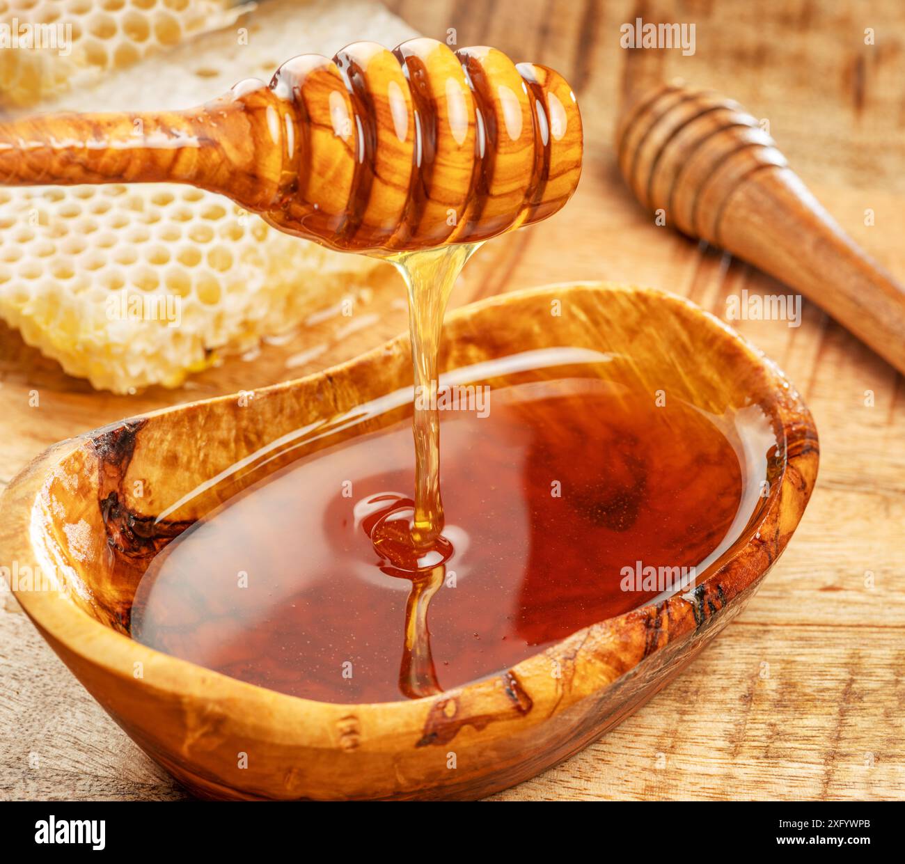Miel biologique naturel dans un bol en bois, plongeur de miel et nids d'abeilles sont à proximité. Banque D'Images