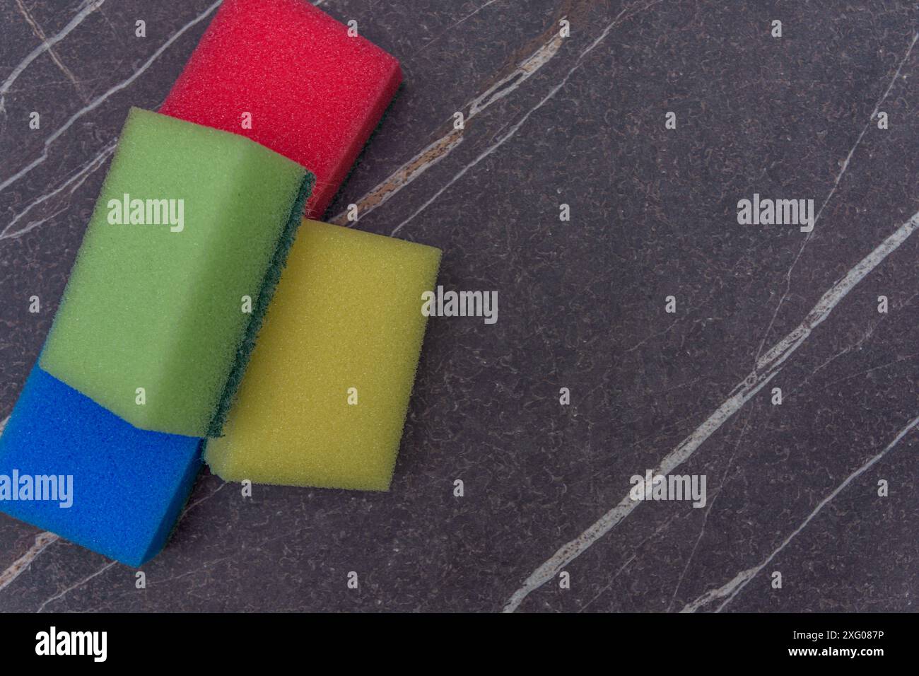 Quatre tampons à récurer de couleurs différentes sur une surface en marbre foncé Banque D'Images