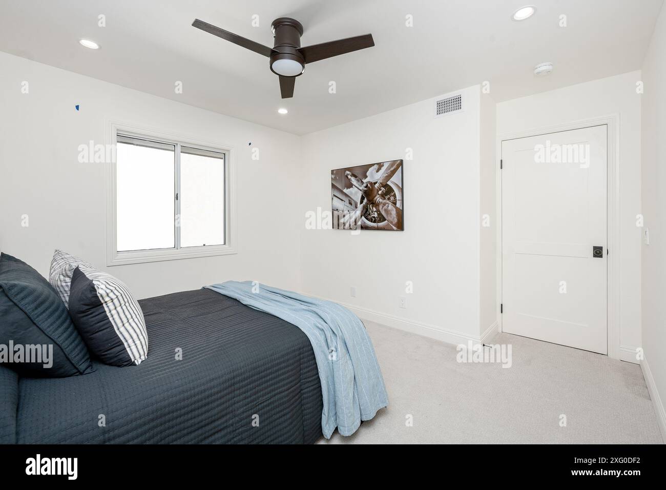 Cette chambre minimaliste dispose d''un ventilateur de plafond moderne, d''un lit simple et d''une fenêtre offrant de la lumière naturelle. Banque D'Images