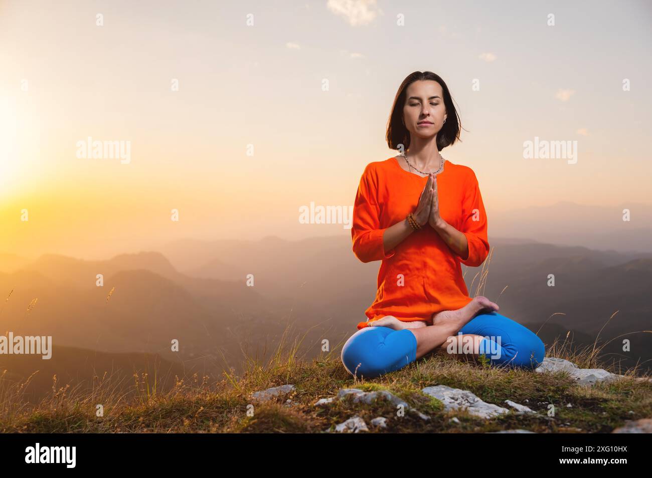 Yogini en position de lotus en plein visage est assis sur une falaise contre la toile de fond du ciel du coucher du soleil avec des montagnes, des prières Banque D'Images