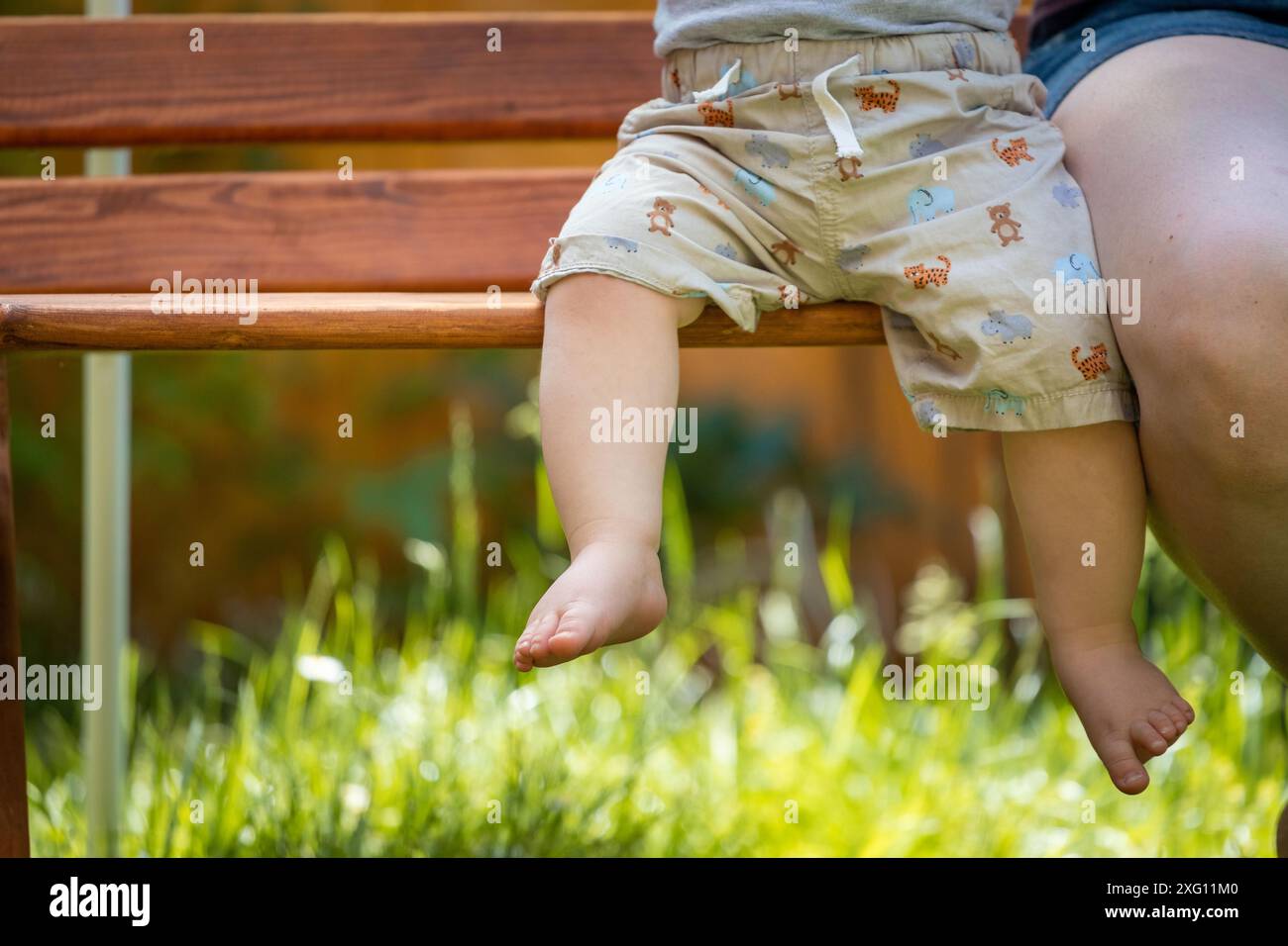 Concept de bébé grandir : gros plan des pieds de bébé pieds nus assis sur le banc du parc, heure d'été Banque D'Images