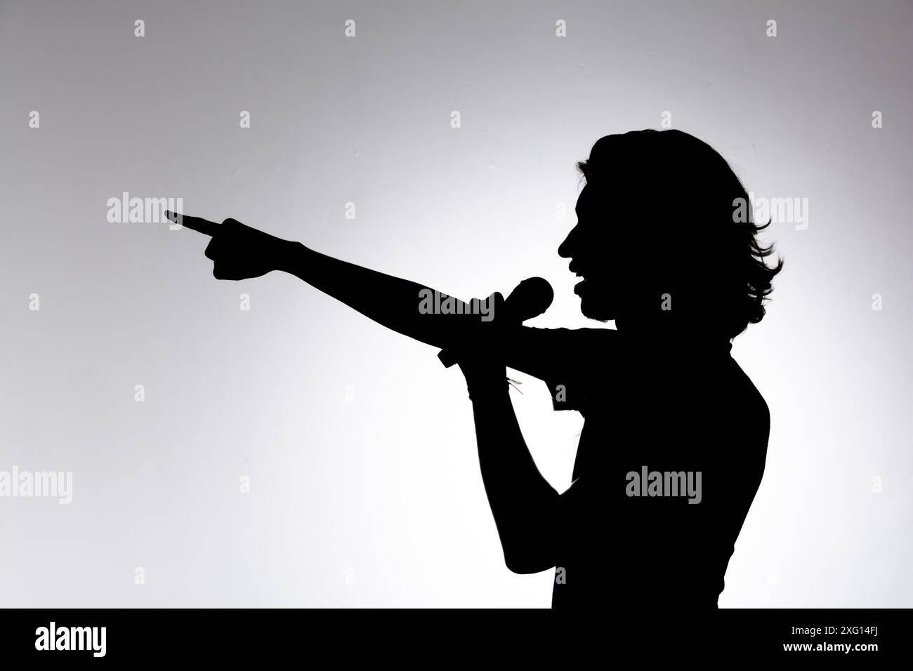 Silhouette d'un jeune homme tenant le microphone sans fil et pointant vers l'avant. Isolé sur fond blanc. Banque D'Images