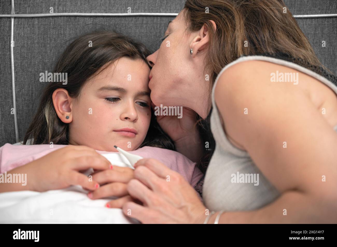 Mère mesurant la température de sa fille malade. Enfant malade ayant une forte fièvre au lit et mère tenant un thermomètre. Photo de haute qualité Banque D'Images