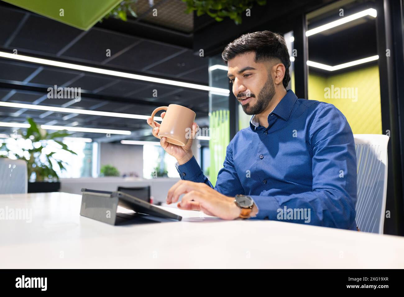 Tenant la tasse à café, homme travaillant sur tablette dans un environnement de bureau moderne, espace de copie Banque D'Images