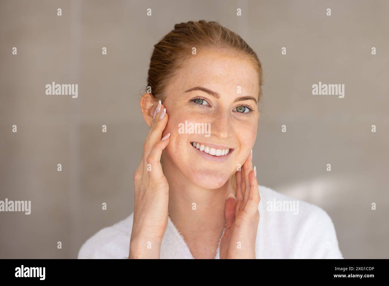 Application de crème pour le visage, femme souriante en robe blanche appréciant la routine de soins de la peau Banque D'Images