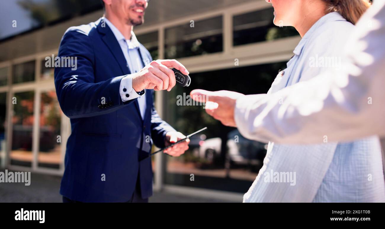 Un vendeur hispanique souriant remet les clés aux propriétaires de voitures neuves chez un concessionnaire local pendant les heures d'ouverture. Banque D'Images Un vendeur hispanique souriant remet les clés aux propriétaires de voitures neuves chez un concessionnaire local pendant les heures d'ouverture. Banque D'Images