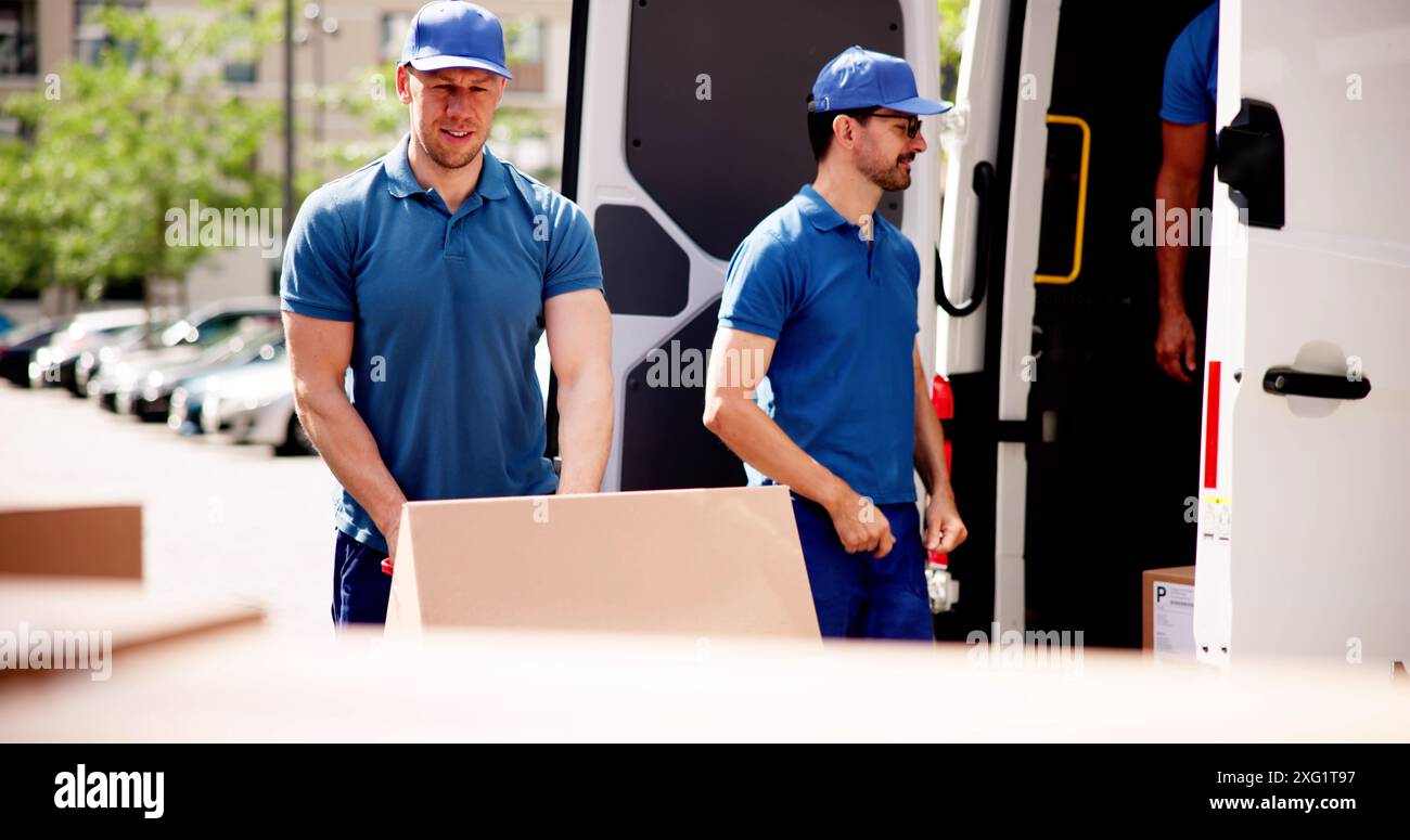 Équipe de livraison efficace transportant des fournitures d'entrepôt : la logistique de la chaîne d'affaires en action avec des déménageurs souriants déchargeant des boîtes en carton du camion Banque D'Images