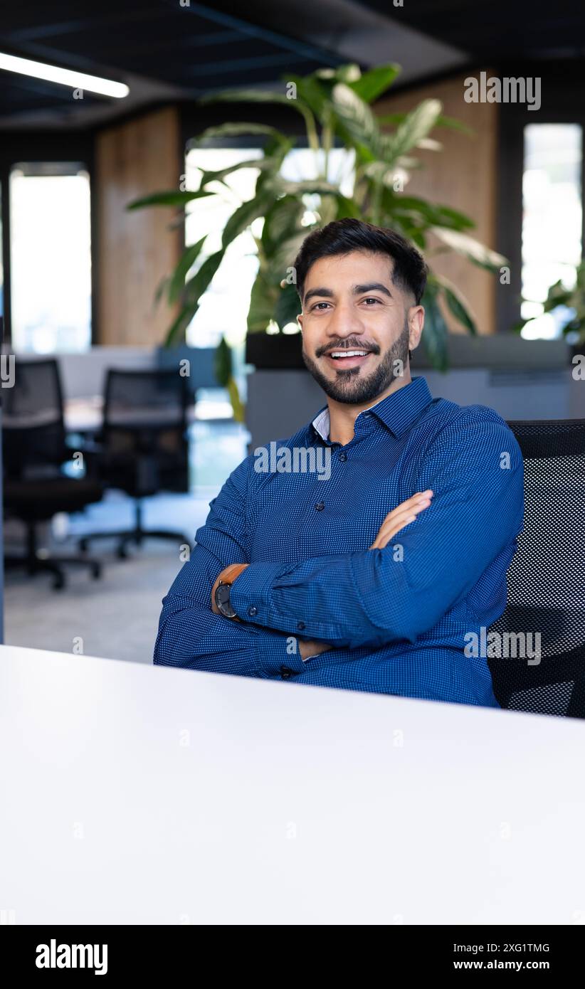 Homme d'affaires souriant au bureau assis au bureau avec les bras croisés, regardant confiant Banque D'Images