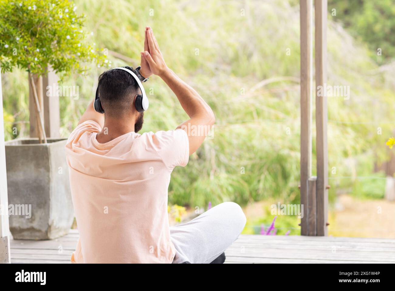 Assis les jambes croisées sur le porche, homme portant des écouteurs méditant à l'extérieur, espace de copie Banque D'Images