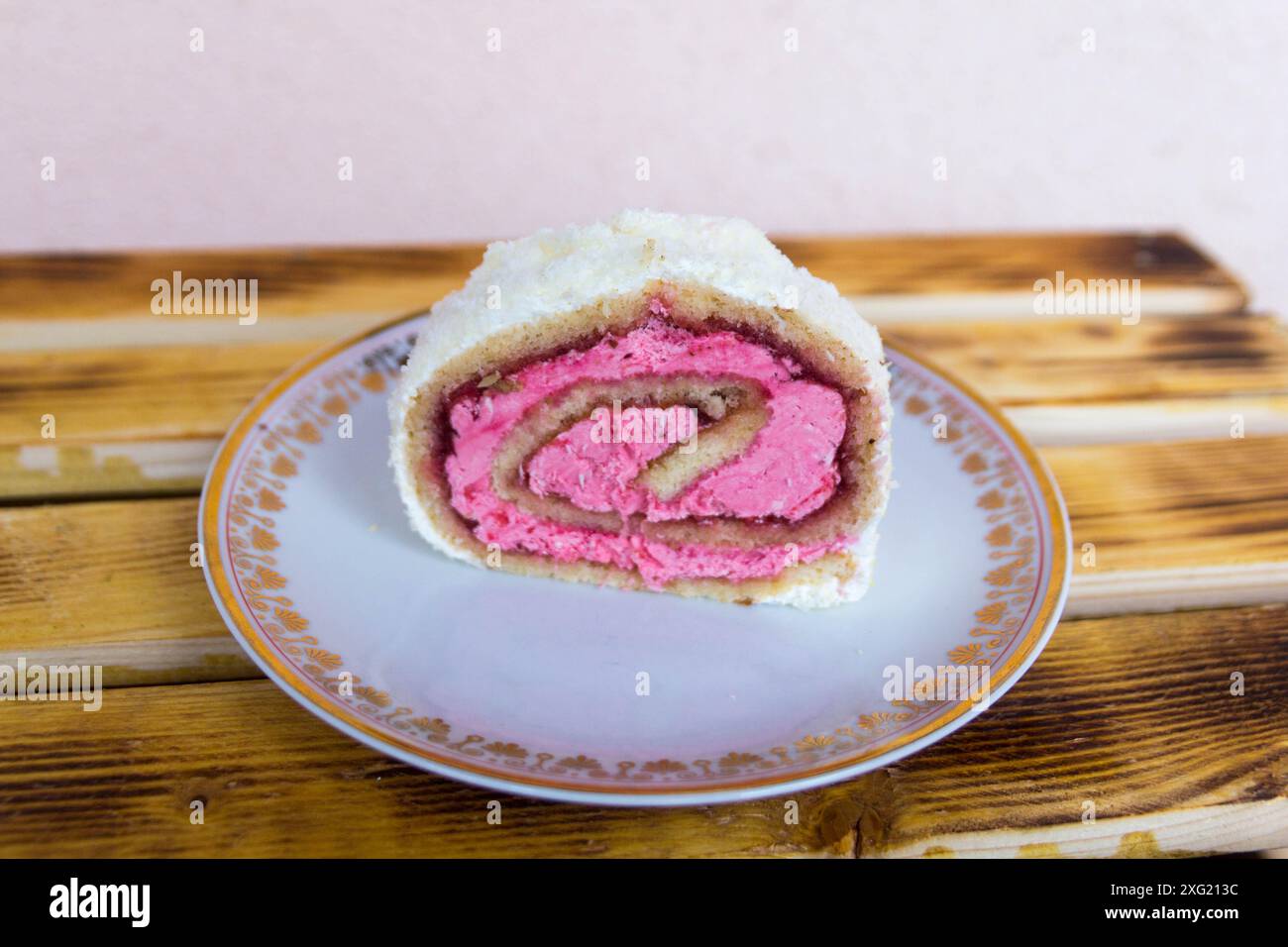 Rouleau suisse fourré de crème rose et garni de noix de coco desséchée servi dans une assiette Banque D'Images