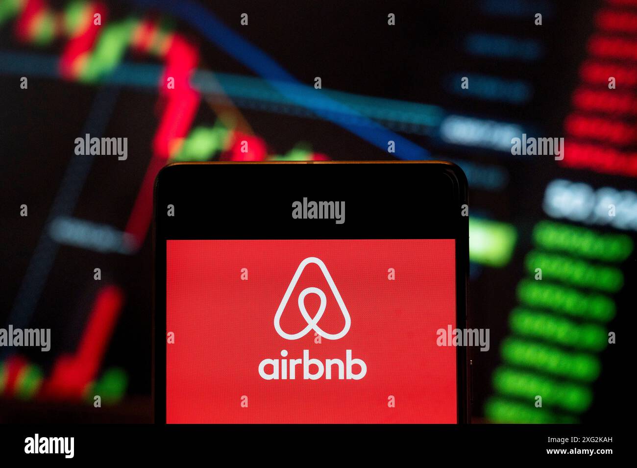 Dans cette illustration photo, le logo de la place de marché en ligne américaine et du service hôtelier Airbnb (NASDAQ : ABNB) vu sur un smartphone avec un graphique de l'indice boursier économique en arrière-plan. Banque D'Images