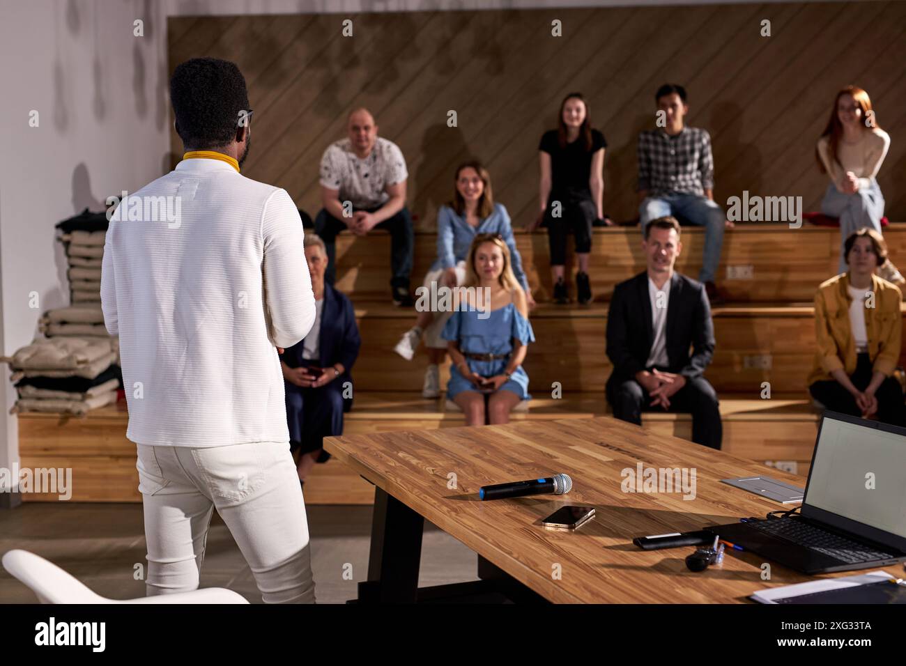 Vue arrière sur jeune enseignant afro-américain donnant un discours aux étudiants adultes l'écoutant attentivement, regardant heureux, Groupe de personnes dans le Backgro Banque D'Images