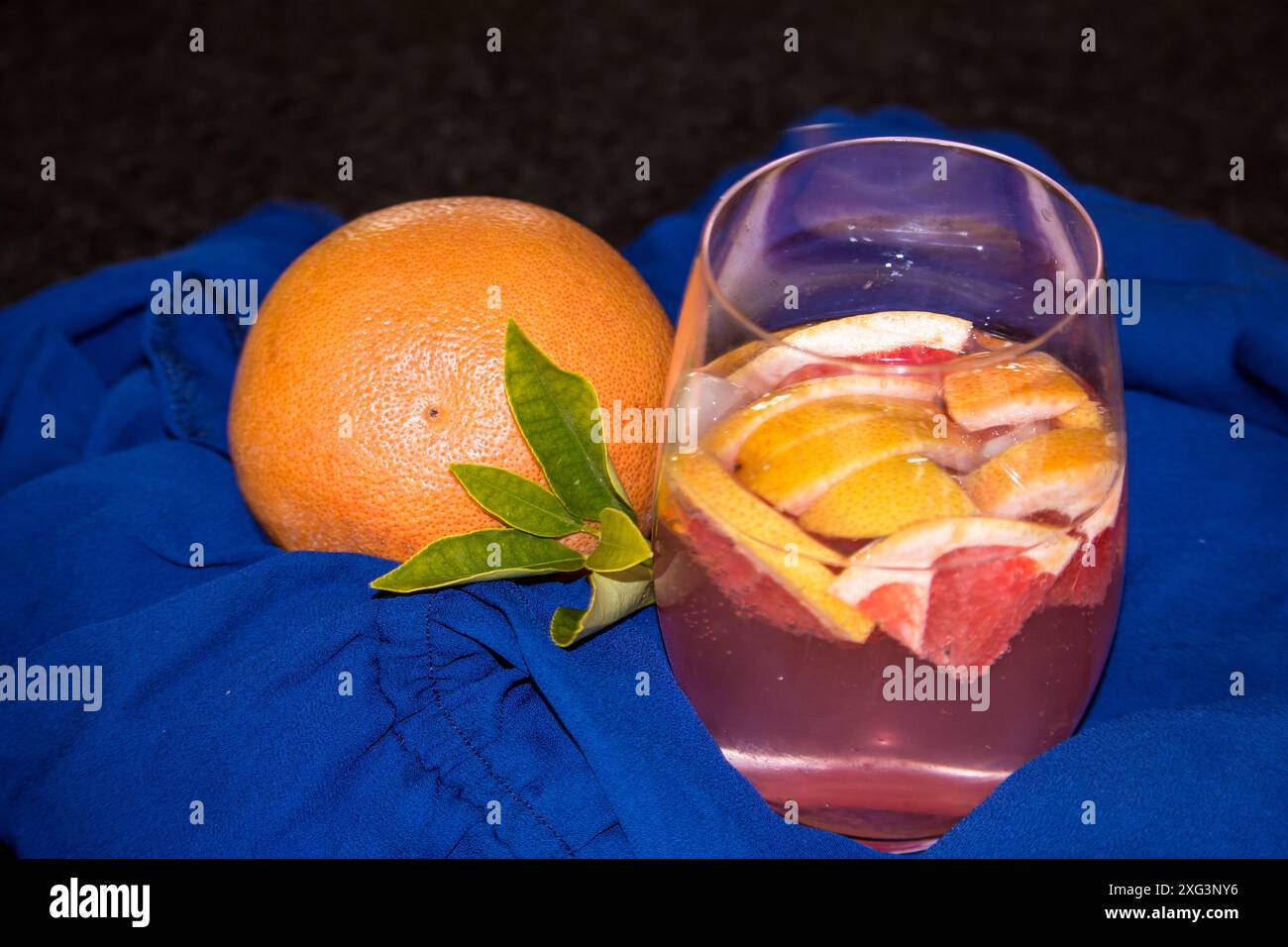 Verre rempli de pamplemousse tranché et d'un gin rose et tonique sur un tissu bleu royal. Banque D'Images