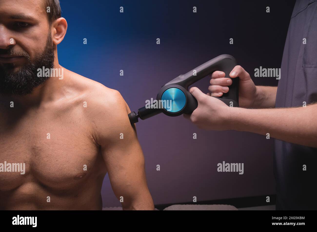 Massage des épaules avec un masseur à percussion dans un salon de massage professionnel. Utilisation comme masseur à percussion dans une pièce sombre Banque D'Images