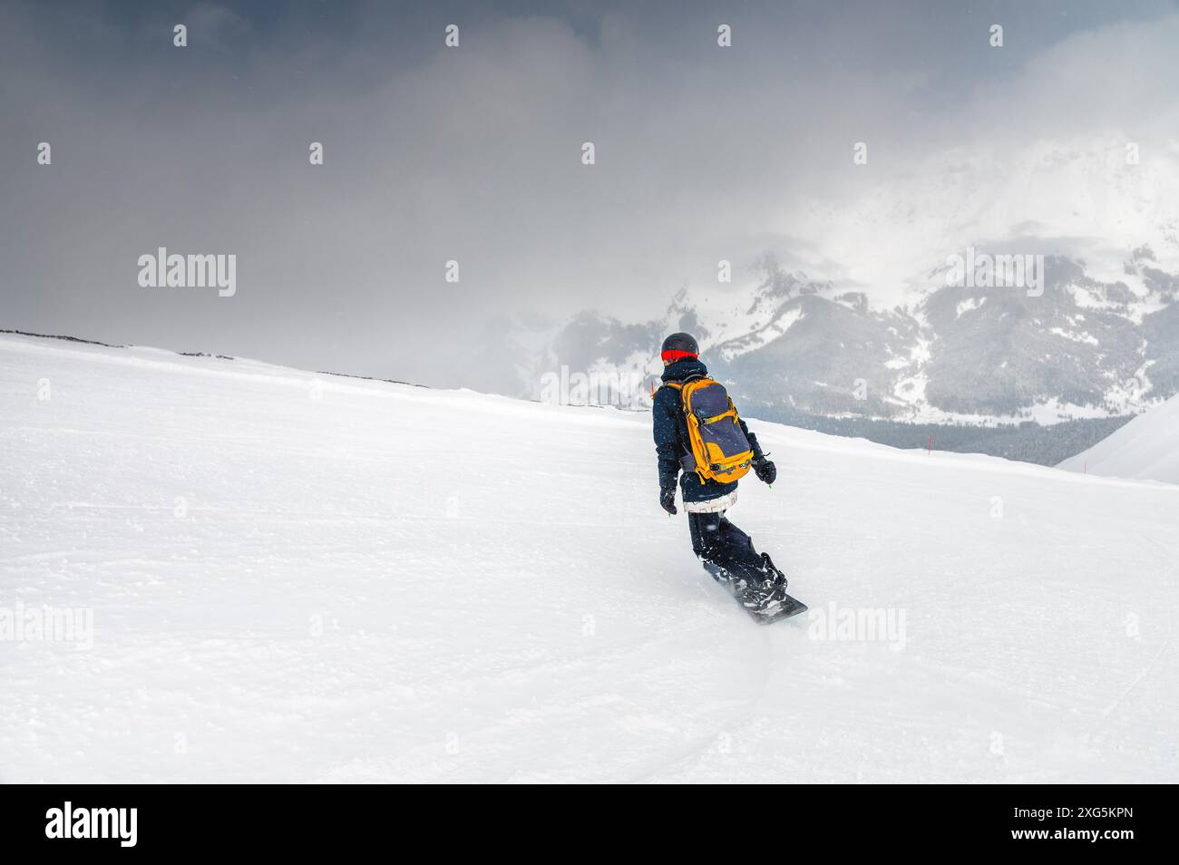 Un jeune snowboarder sportif monte sur une pente enneigée contre la toile de fond des montagnes lors d'une journée d'hiver dans une station de ski Banque D'Images