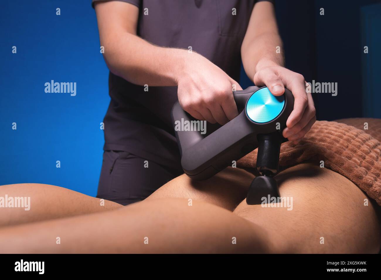 Gros plan du masseur masculin professionnel méconnaissable massant les muscles du mollet de la jambe à l'aide de l'outil de percussion du pistolet de massage de l'homme d'athlète musculaire, sur le spa Banque D'Images