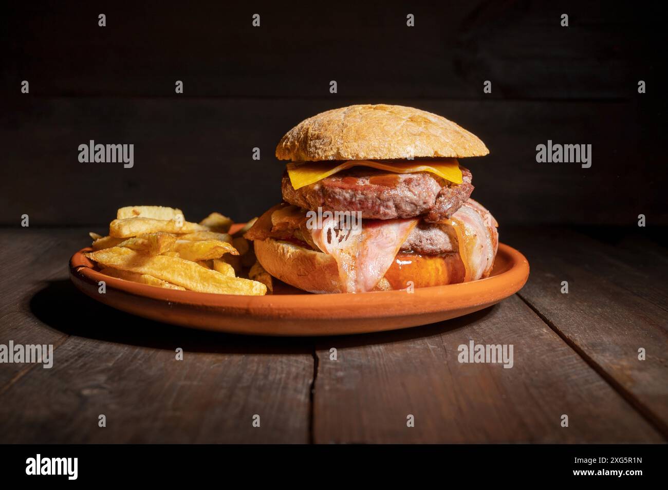 Hamburger de bœuf grillé de qualité supérieure avec bacon, fromage et frites. Délicieux hamburger américain sur fond de bois. Photographie de haute qualité Banque D'Images