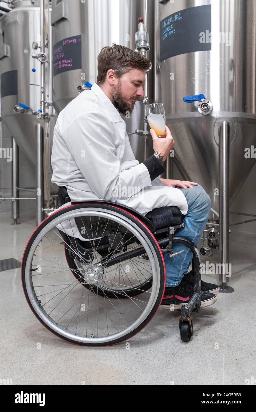 Personne handicapée qui utilise un fauteuil roulant travaillant à l'usine de bière artisanale. Photographie de haute qualité Banque D'Images