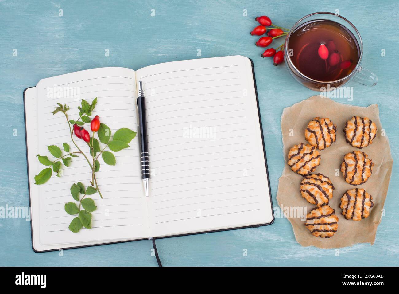 Macarons à la noix de coco sur un fond bleu texturé, livret vide avec un stylo, tasse de thé avec rose hanche rouge Banque D'Images