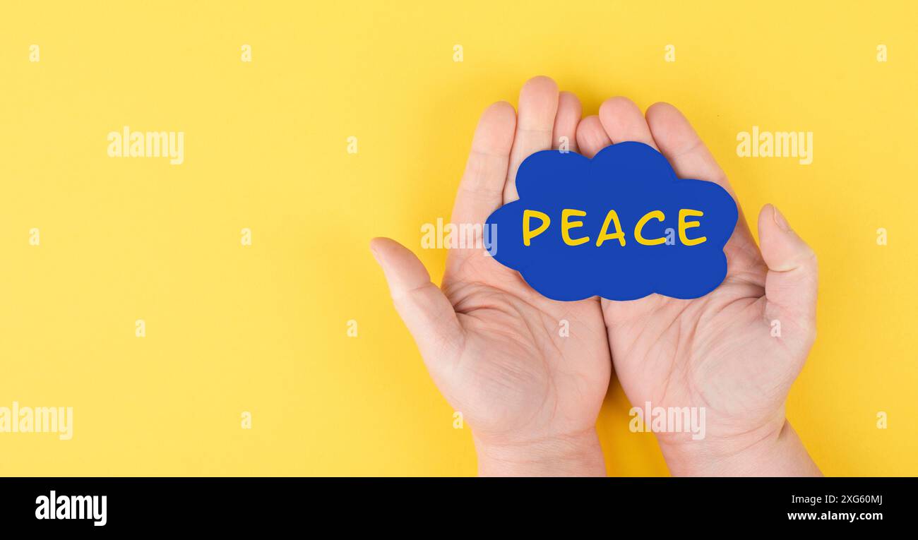 Tenir un nuage bleu avec le mot paix entre les mains, mettre fin à la guerre, soutenir l'Ukraine, vivre ensemble pacifiquement, couleur du drapeau ukrainien Banque D'Images