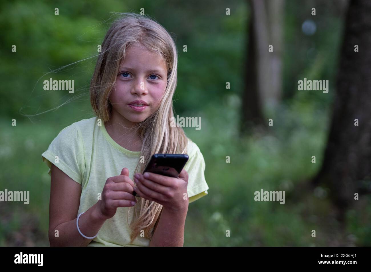 Portrait d'une jeune fille jolie aux longs cheveux blonds. L'enfant est allongé dans l'herbe d'un parc, profitant de la nature, de la santé, de la liberté et de son téléphone portable Banque D'Images