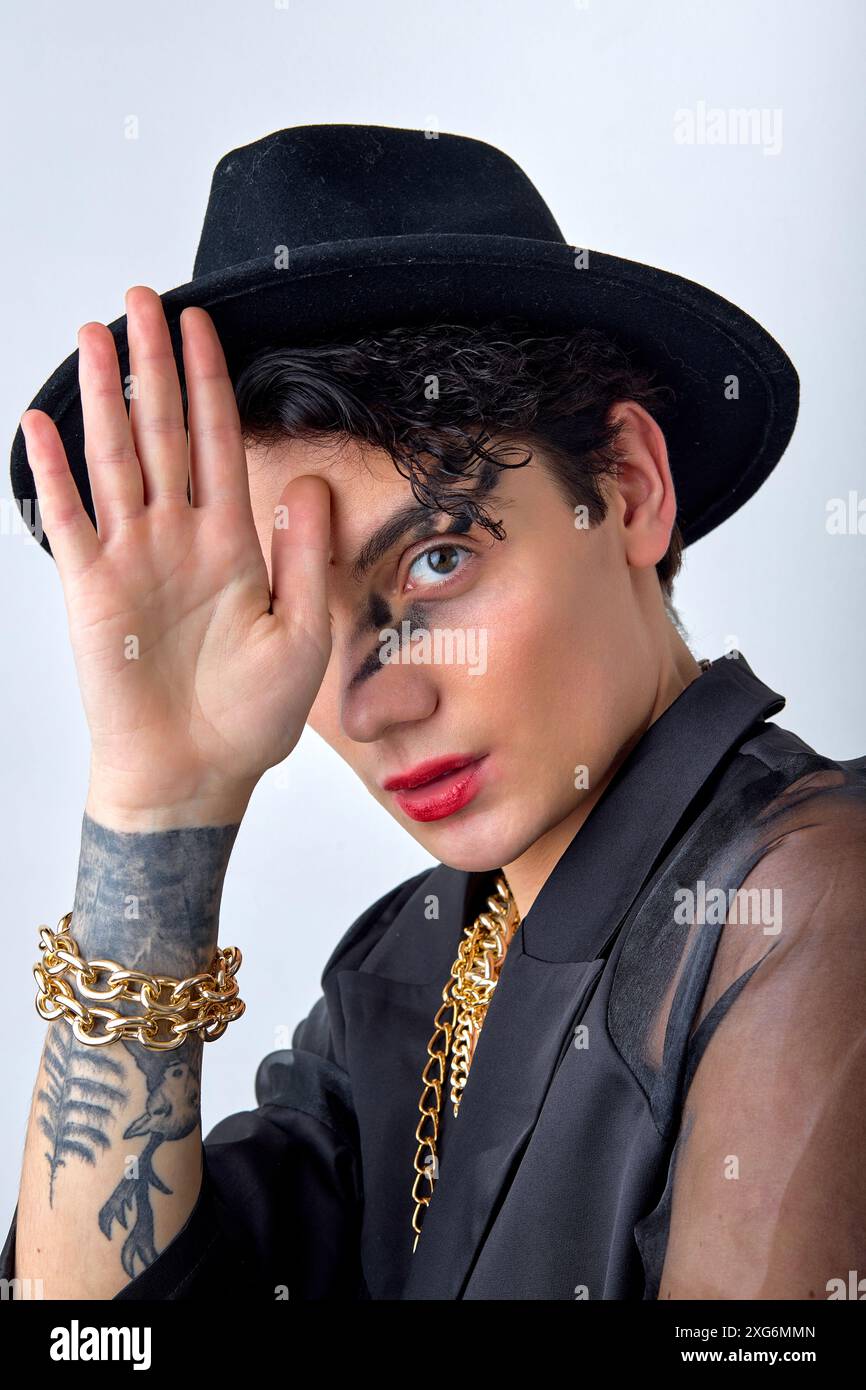 Portrait de visage de l'homme gay glamour 20s porter chemise noire et chapeau élégant, maquillage regardant la caméra isolé sur fond blanc studio. lgb homosexuel Banque D'Images