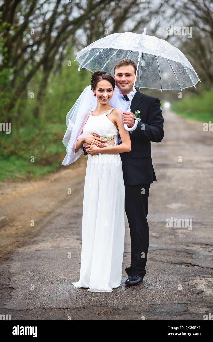mariée et marié le jour d'un mariage pluvieux marchant sous un parapluie Banque D'Images