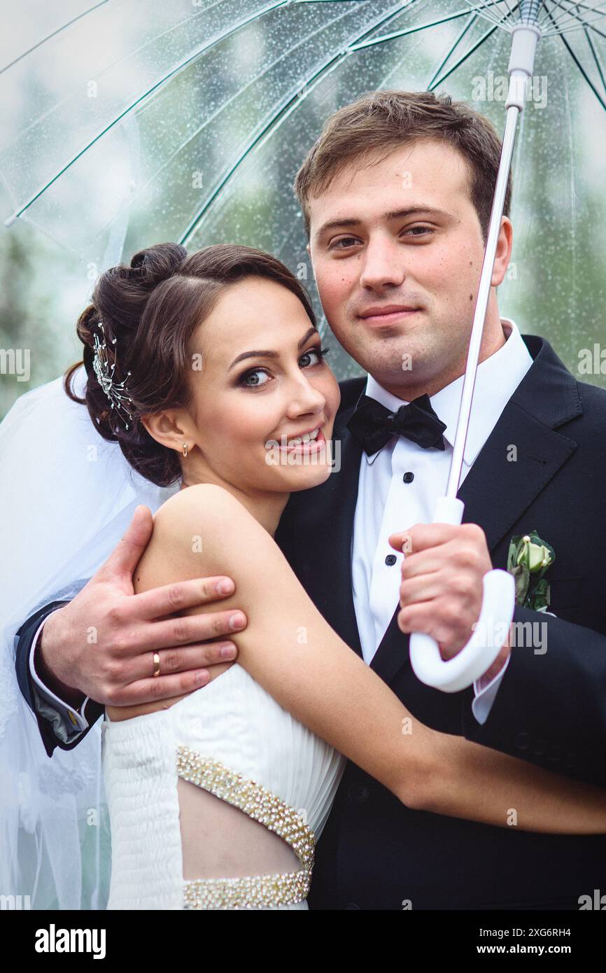 mariée et marié le jour d'un mariage pluvieux marchant sous un parapluie Banque D'Images