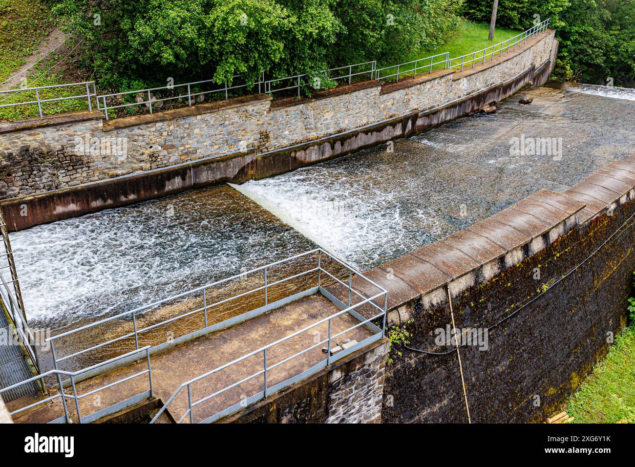 Déversoir auxiliaire en escalier sur le barrage de Robertville avec de l'eau qui coule dans la rivière Warche, arbres verts en arrière-plan flou, jour nuageux à Waimes, Belgique Banque D'Images