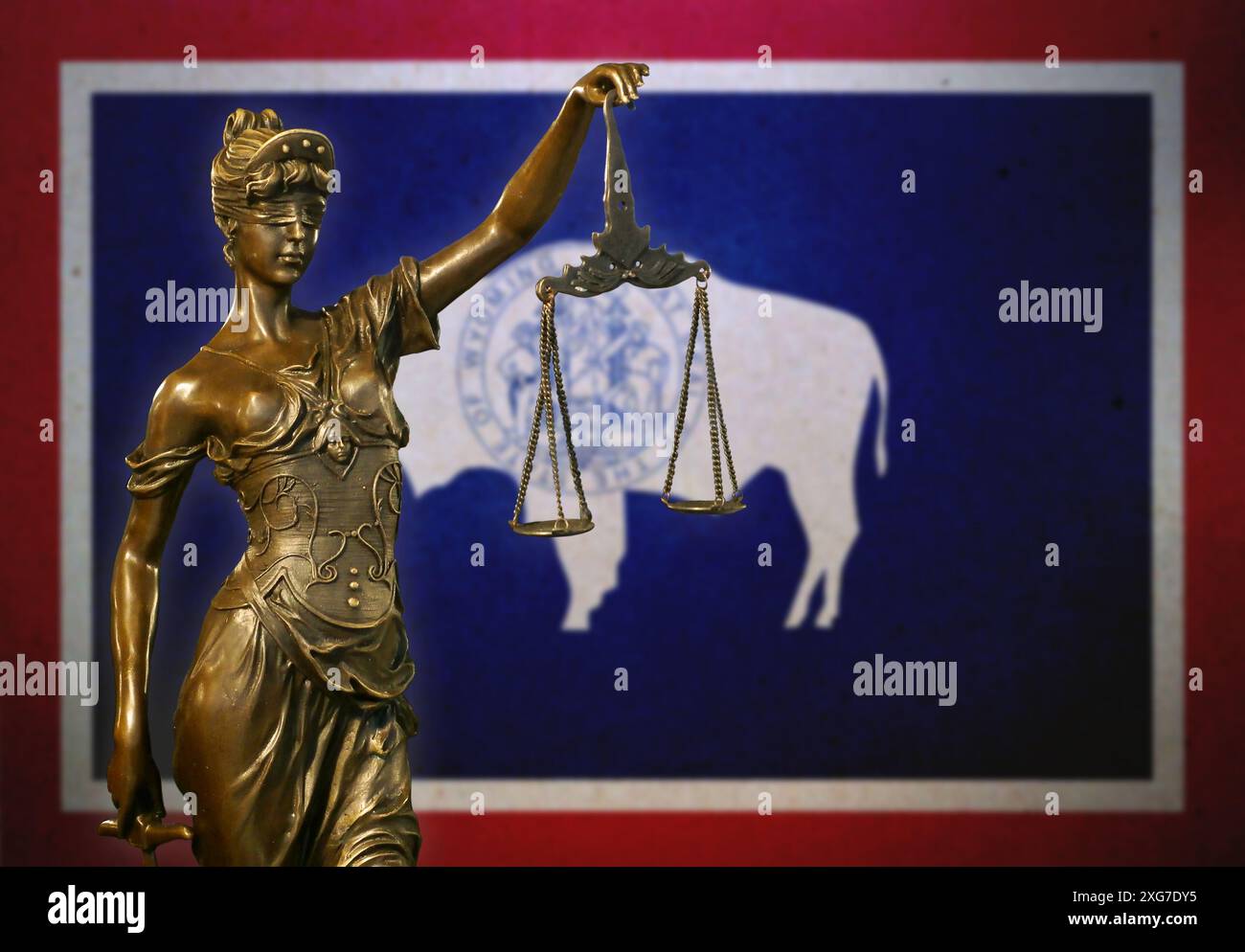 Gros plan d'une petite statuette en bronze de Lady Justice devant un drapeau du Wyoming. Banque D'Images