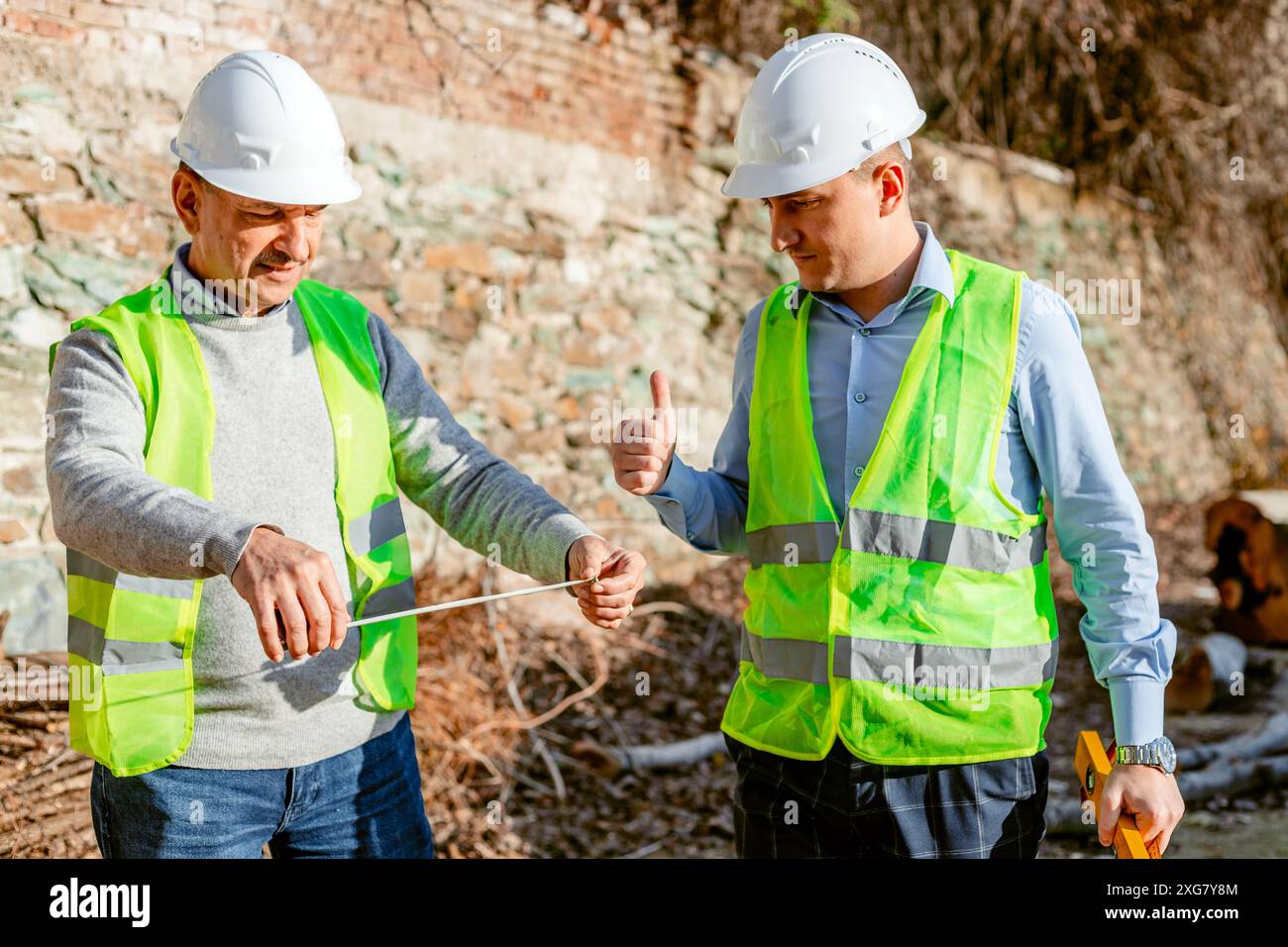 Deux ouvriers de la construction portant des gilets de sécurité et des casques de sécurité mesurent une distance sur un chantier de construction. Banque D'Images