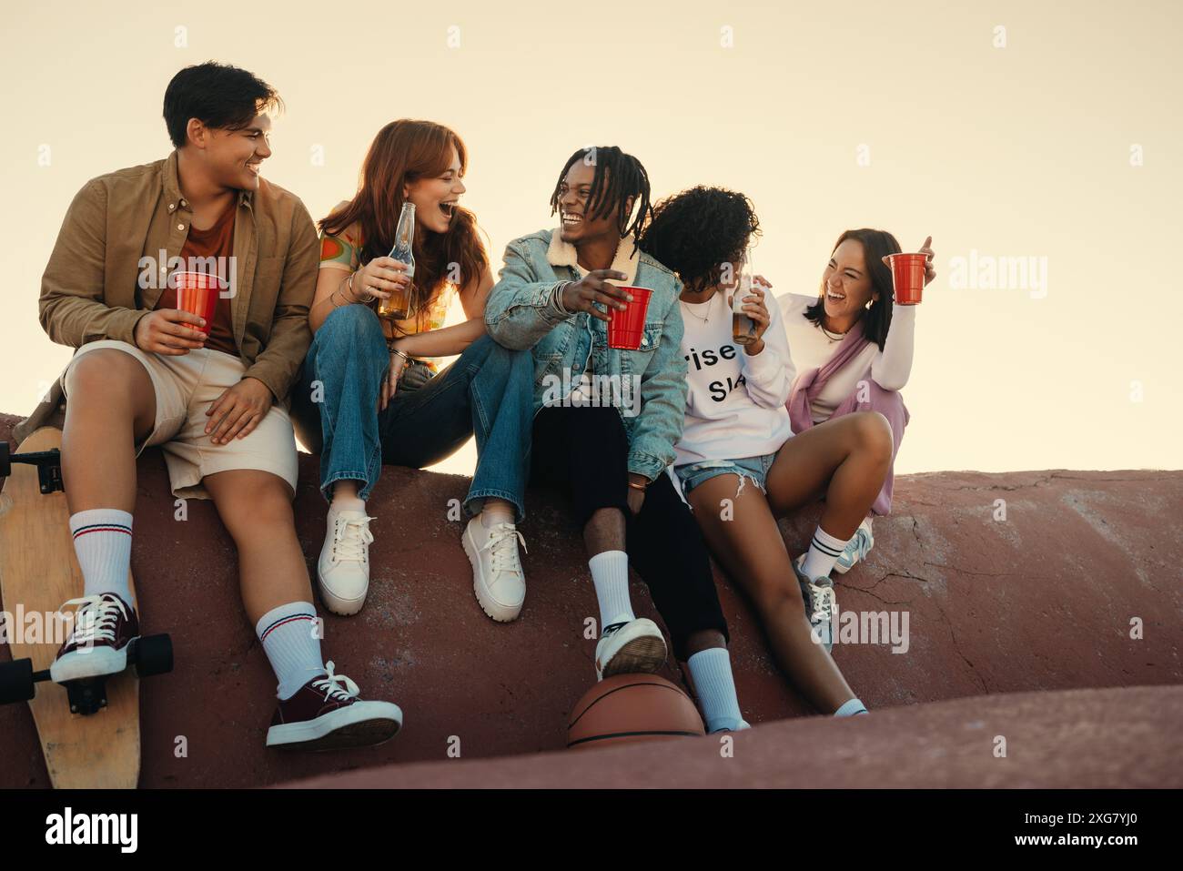 Groupe d'amis s'amusant et riant ensemble tout en profitant d'un verre à l'extérieur, capturant des moments de joie et de camaraderie. Banque D'Images