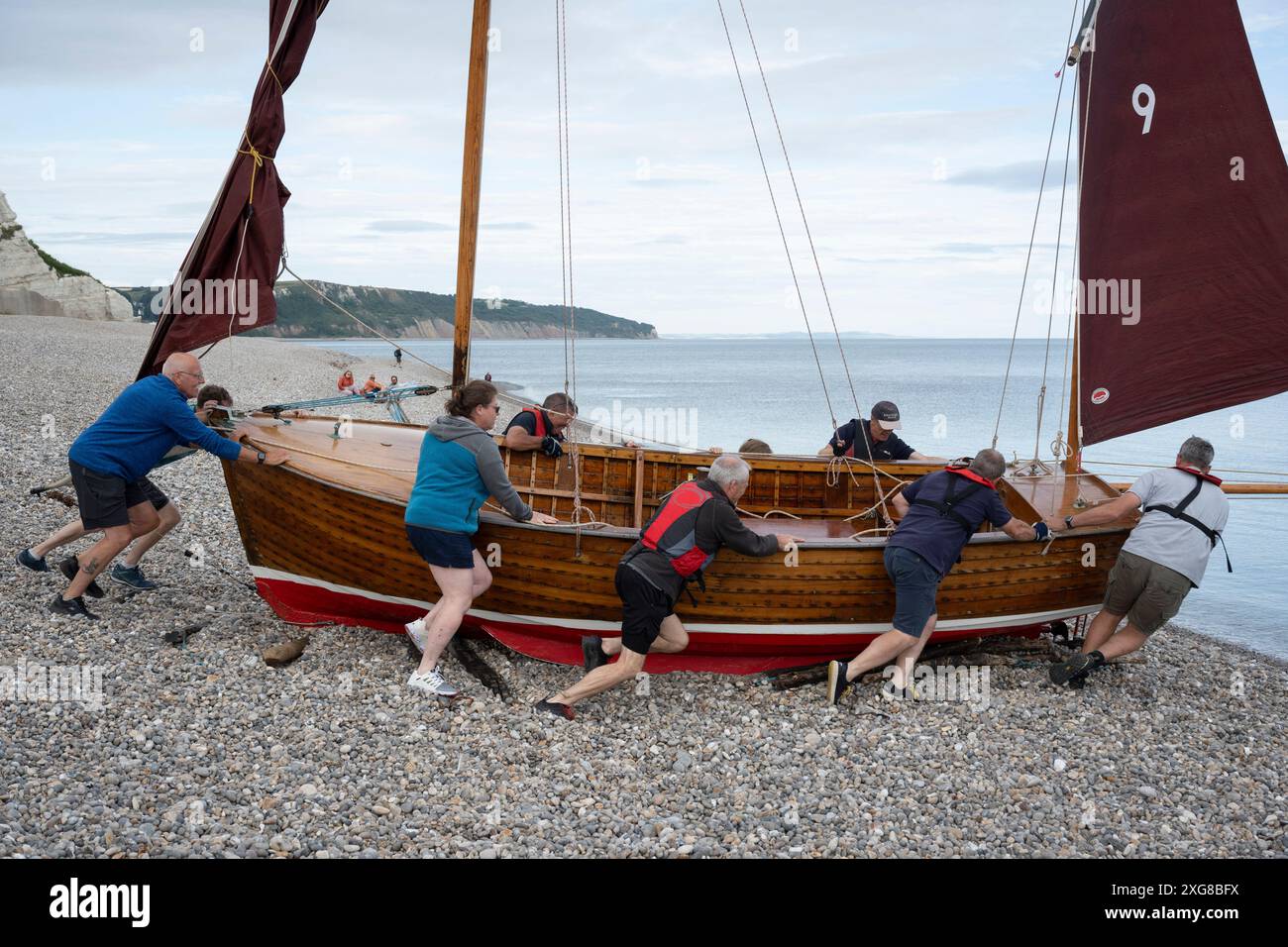 Les membres du Beer Luggers Club lancent leurs bateaux lugger vieux de 50-60 ans depuis la plage de galets pour une course entre les bouées voisines au large de la côte est du Devon, le 1er juillet 2024, à Beer, Devon, Angleterre. Banque D'Images