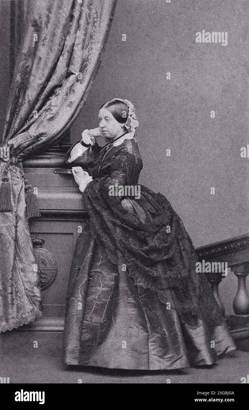 La reine Victoria, impératrice de l'Inde, se tient dans une pose majestueuse, sa main gauche reposant sur un pilier drapé de tissu à motifs, tandis qu'elle regarde sur le côté. Elle porte une robe sombre volumineuse et un bonnet en dentelle sur ses cheveux. Ce portrait photographique a été réalisé en 1861. Banque D'Images