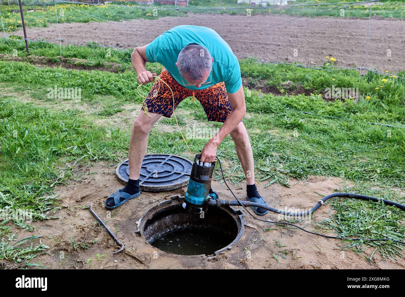 L'homme abaisse la pompe d'eaux usées submersible dans la fosse septique. Banque D'Images