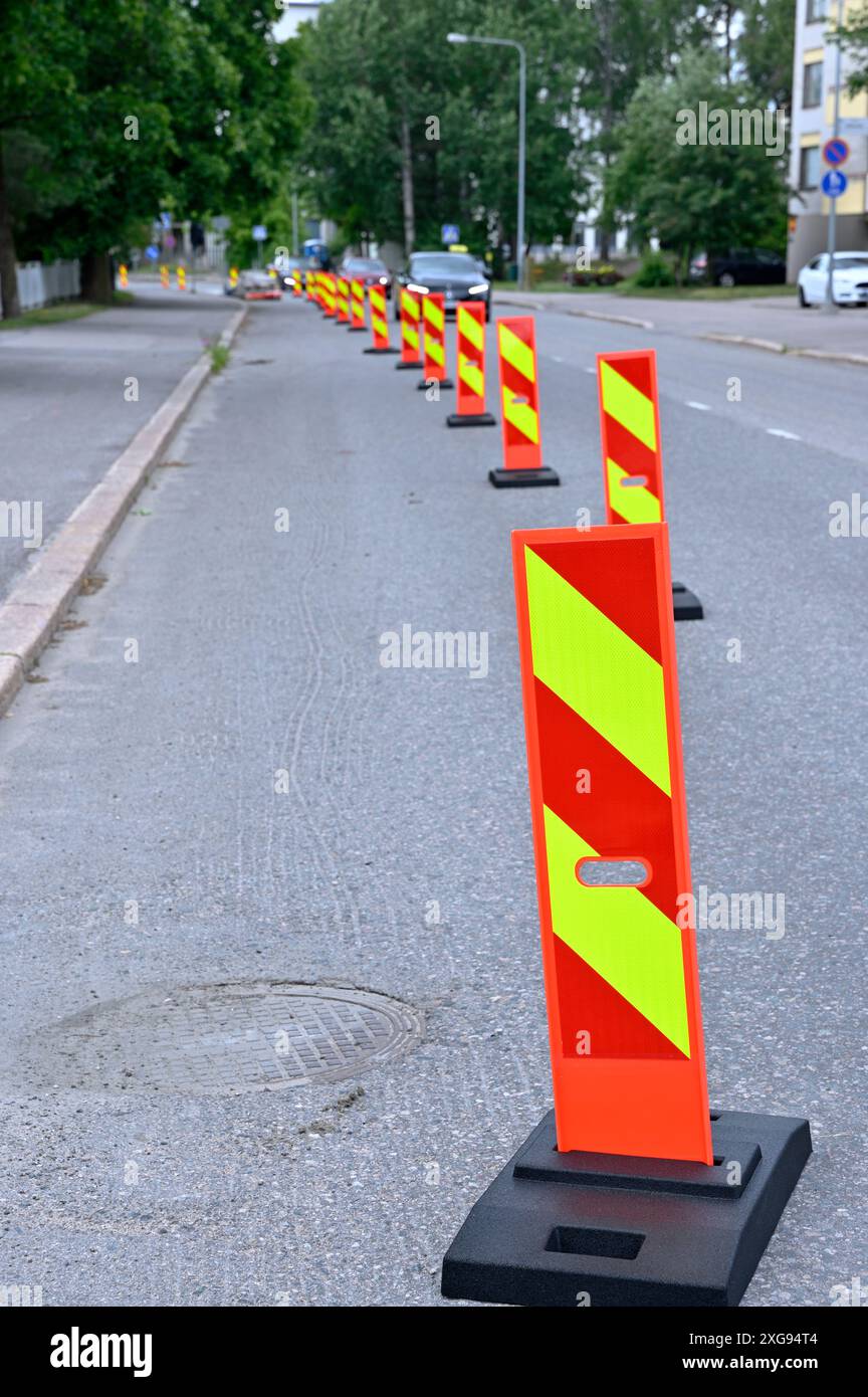 Une rangée de barrières de circulation réfléchissantes orange vif et jaune alignées le long d'une rue de la ville pour marquer une zone de construction. Les barrières sont positionnées à Banque D'Images