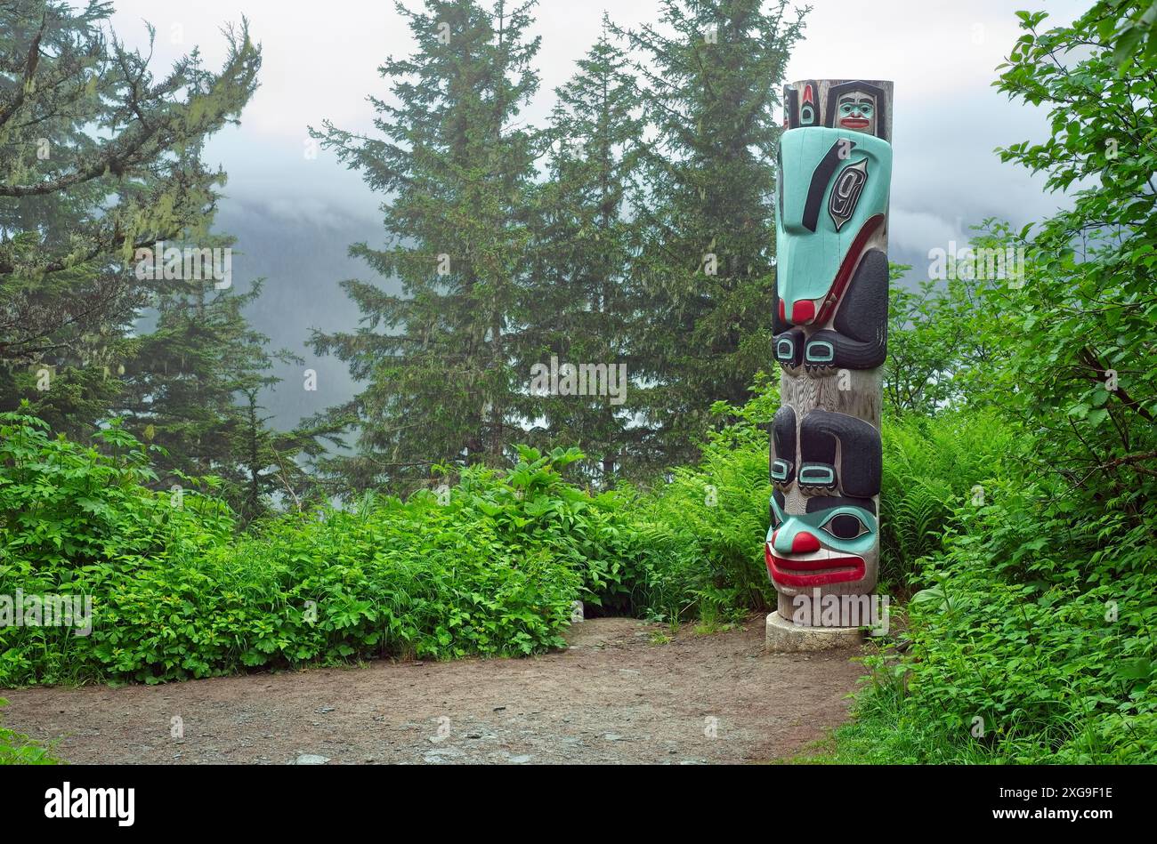 Un totem se tient près d'un sentier à travers une forêt brumeuse sur une montagne au-dessus de Juneau, Alaska Banque D'Images