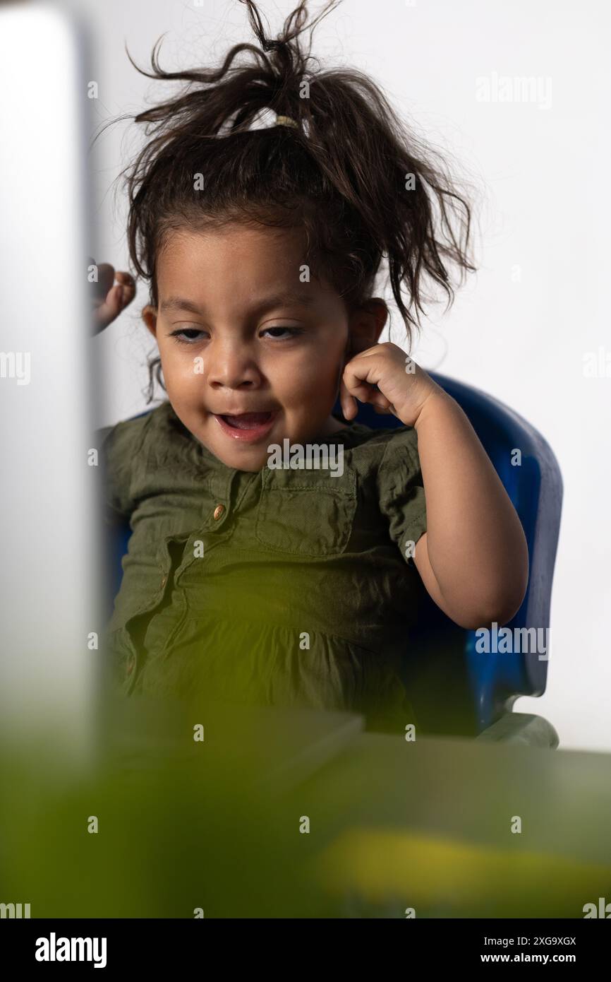 Belle fille latine de 2 ans assise bâillant, devant l'ordinateur portable Banque D'Images